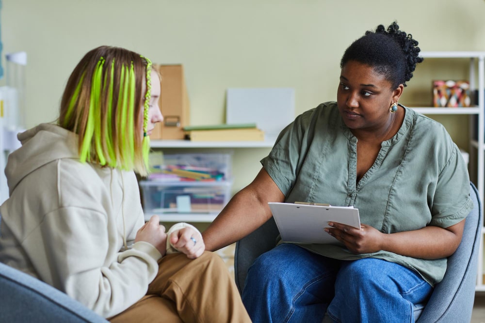 african female school psychologist supporting sad teenage girl during her difficult situation school min